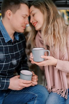 Smiling man and woman touching foreheads while sitting with cups in their hands. High quality photo