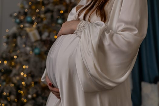 Pregnant woman holding a belly against Christmas tree with lights. family holiday concept