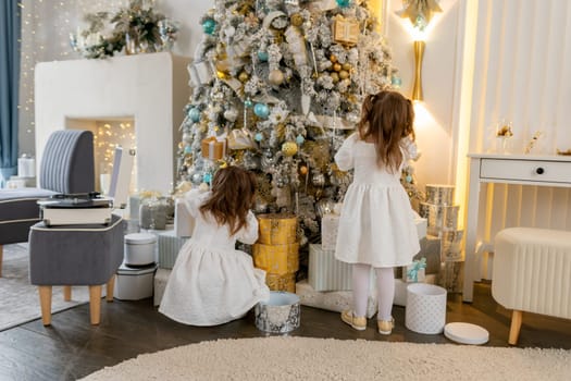 Two twin sisters in a white dress decorate the Christmas tree with their own hands, Christmas holidays at home