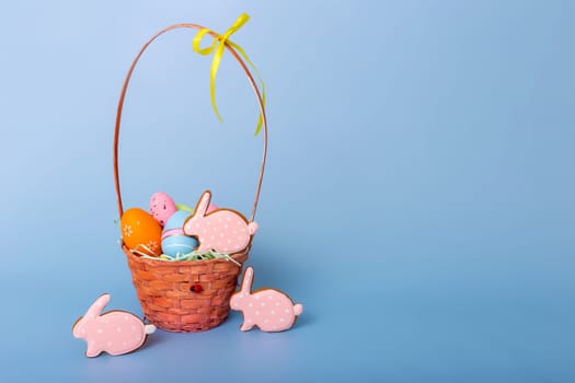 Cute pink gingerbread in the form of a rabbit and a basket with decorative Easter eggs stand on a blue background