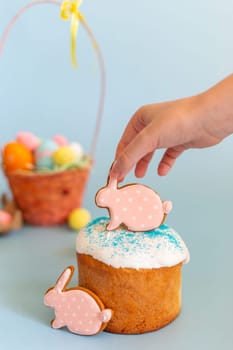 A childs hand holds a pink gingerbread in the shape of a rabbit on an Easter cake. Vertical