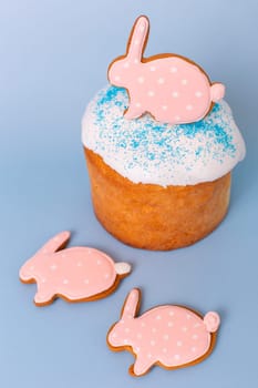 Close up of cute pink gingerbreads in the form of a rabbit on Easter cake, decorative eggs, stand on a blue background.