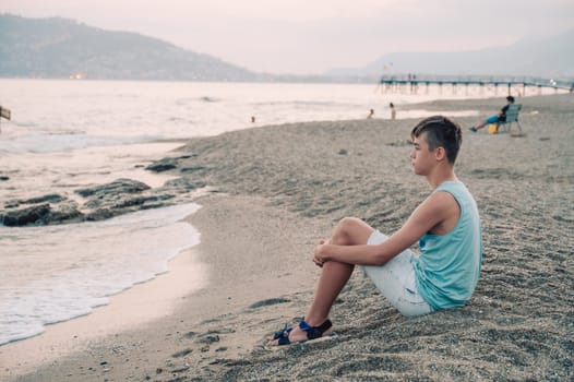 Boy teen sits on the beach and looks at the sea in Alanya city, Turkey. Travelling or vacation concept