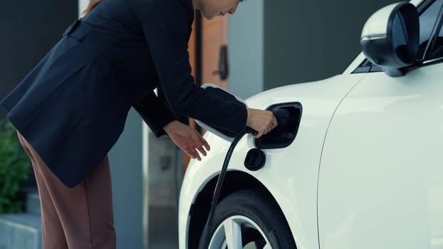 A woman unplugs the electric vehicle's charger at his residence. Concept of the use of electric vehicles in a progressive lifestyle contributes to a clean and healthy environment.