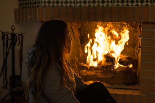 latin woman sitting in front of the fireplace in the cold winters, engrossed in the flames