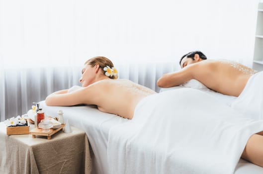 Blissful couple customer having exfoliation treatment in luxury spa salon with warmth candle light ambient. Salt scrub beauty treatment in health spa body scrub. Quiescent