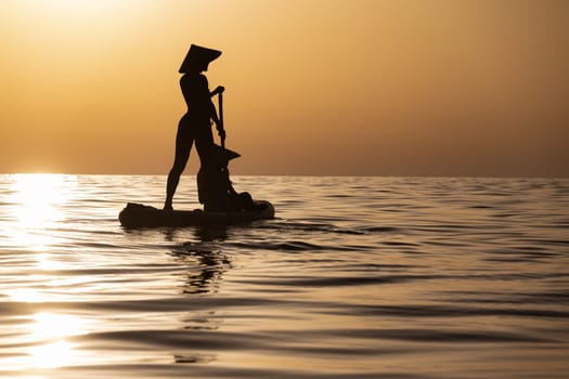 woman with a child on a sup board in the sea swim against the background of a beautiful sunset, Standup paddleboarding