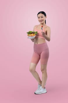 Young sporty Asian woman in sportswear holding salad bowl fill with vibrant of fruit and vegetable. Natural youthful and fit body lifestyle with balance nutrition on isolated background. Vigorous