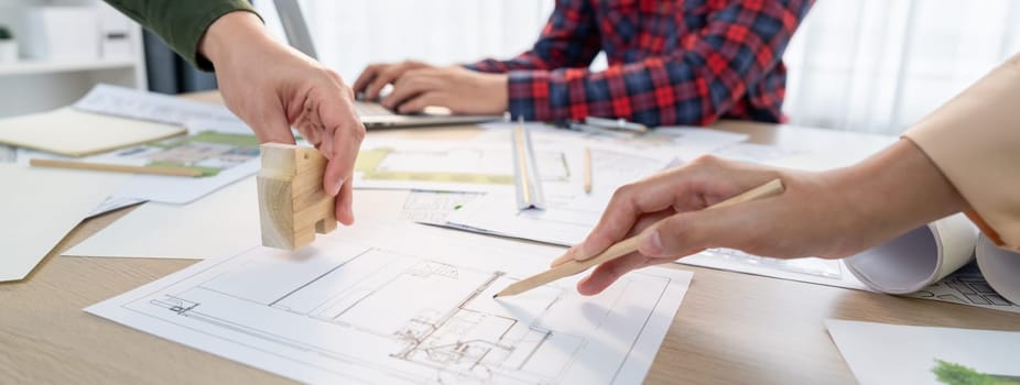 Skilled architect team using architectural equipment during colleague discussion about building design at meeting table with blueprint scatter around. Closeup. Focus on hand. Delineation.