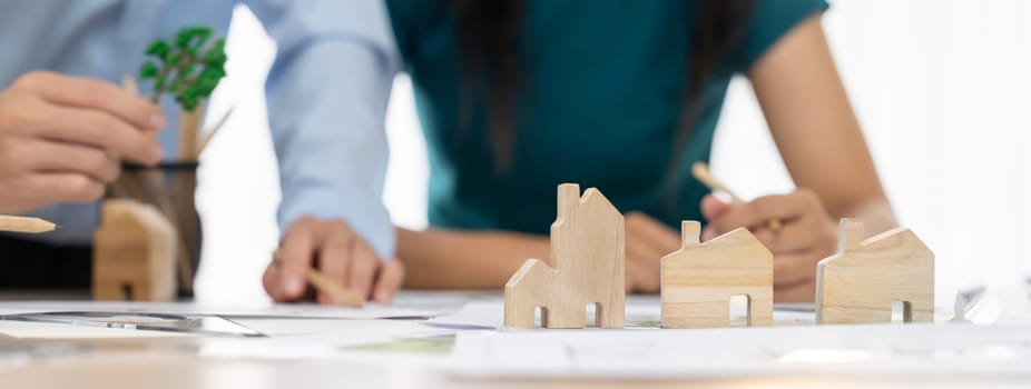 Professional architect engineer team discussion about architectural project on meeting table with wooden block and blueprint scatter around. Design and cooperate concept. Closeup. Delineation.