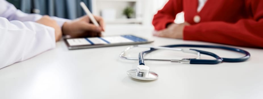 Focused stethoscope on office desk with blurred background of patient attending to doctor appointment at clinic or hospital discussing medical treatment or examining symptoms. Panorama Rigid