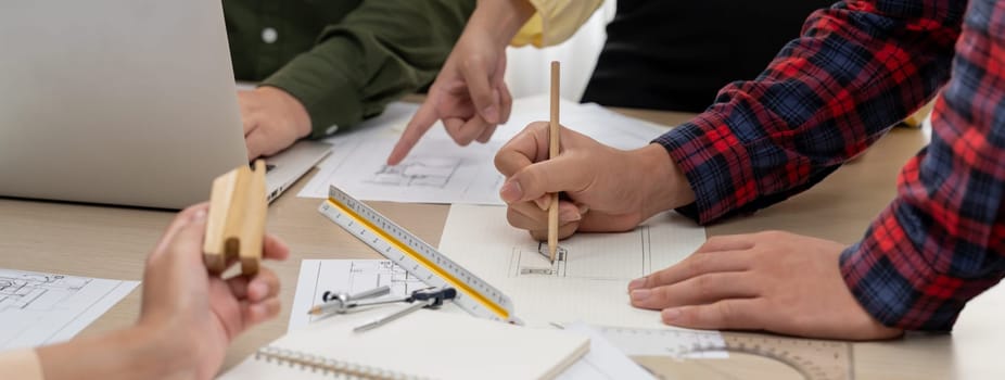 Professional architect team discussion about architectural project on meeting table with blueprint and wooden block scatter around at modern office. Closeup. Focus on hand. Delineation.