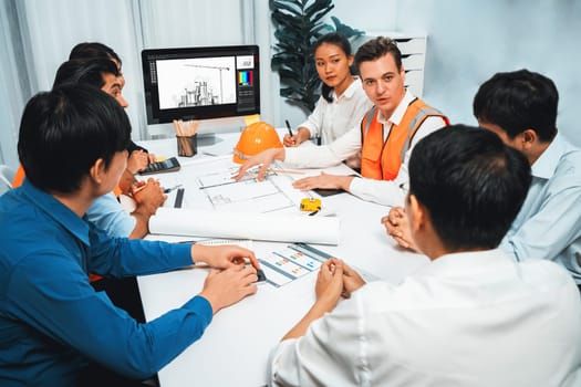 Diverse group of civil engineer and client working together on architectural project, reviewing construction plan and building blueprint at meeting table. Prudent