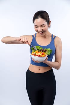 Young sporty Asian woman in sportswear holding salad bowl fill with vibrant of fruit and vegetable. Natural youthful and fit body lifestyle with balance nutrition on isolated background. Vigorous