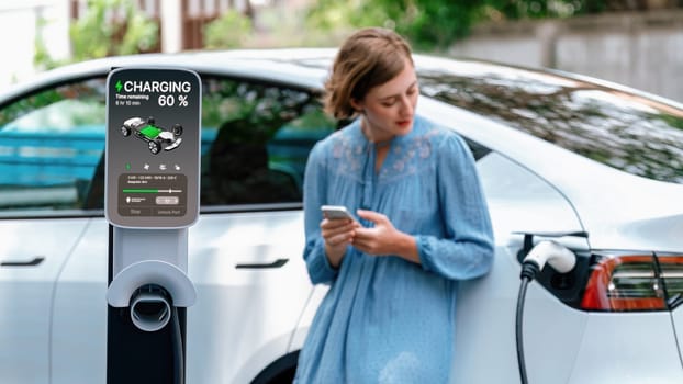 Electric vehicle recharging battery from home EV charging station using alternative energy with net zero emission on blurred background of young girl charging her car before vacation travel. Perpetual