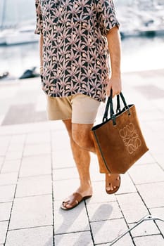 Man in shorts with a beach bag walks on the tiles in the yard. Cropped. Faceless. High quality photo