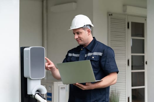 Qualified technician working on home EV charging station installation, making troubleshooting and configuration setup on charging system with laptop for EV at home. Synchronos