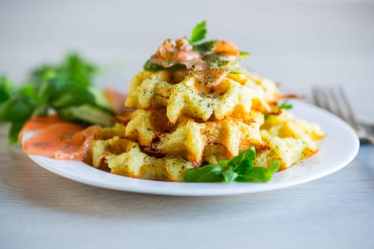 Cooked potato waffles with lightly salted red fish and herbs in a plate, on a wooden table.