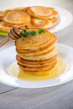 cooked sweet pancakes with honey in a plate on a light wooden table.