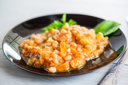 Cooked white beans with zucchini and other vegetables, on a wooden table.