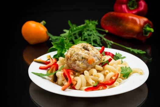 cooked pasta with meatballs, peppers and herbs with spices in a plate, isolated on a black background