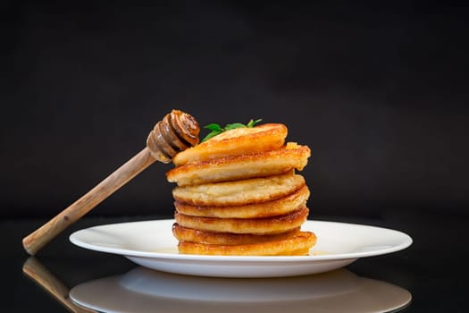 cooked sweet pancakes with honey in a plate isolated on black background