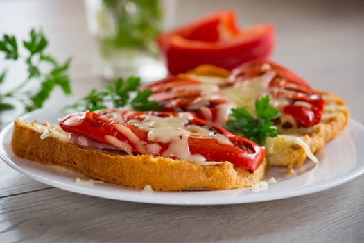 hot sandwich of fried toast bread with baked peppers and cheese, in a plate on a wooden table