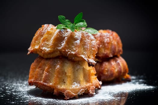 cooked sweet honey muffins in powdered sugar isolated on black background