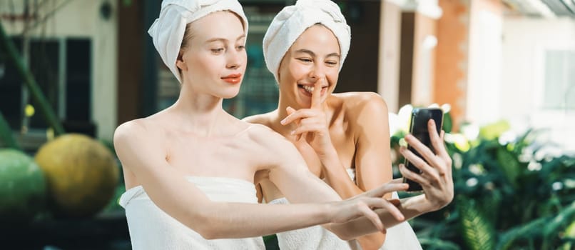 Couple of young beautiful women with beautiful skin in white towel taking a photo together at outdoor surrounded by peaceful natural environment. Beauty and healthy spa concept. Tranquility.