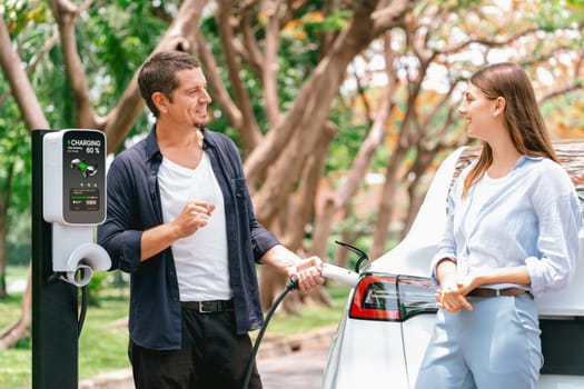 Lovely young couple recharging battery for electric car during autumnal road trip travel EV car in autumnal forest. Eco friendly travel on vacation during autumn. Exalt