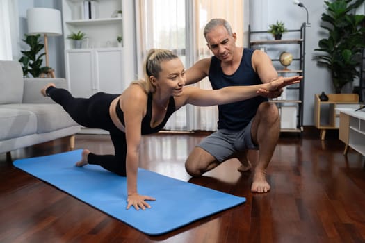 Happy active senior couple in sportswear being supportive and assist on yoga posture together at home. Healthy senior man and woman lifestyle with yoga exercise. Clout