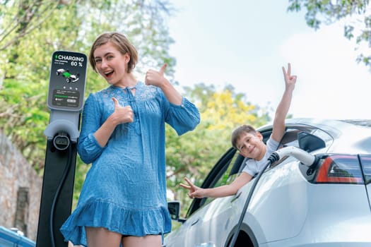 Family road trip vacation with electric vehicle, mother and son recharge EV car with green and clean energy. Nature and travel with eco-friendly car for sustainable environment. Perpetual