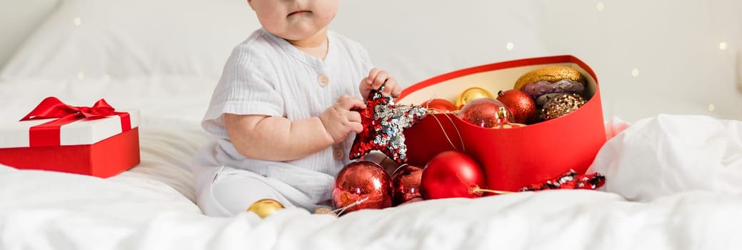 Christmas Baby in Santa Hat, Child holding christmas bauble near Present Gift Box over Holiday Lights