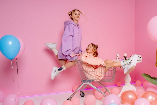 Two beautiful attractive funny joyful cheerful relaxed carefree girls dressed in casual fashion clothes isolated on hot pink background.