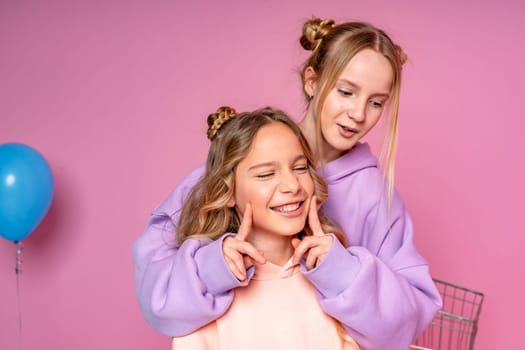 Two beautiful attractive funny joyful cheerful relaxed carefree girls dressed in casual fashion clothes isolated on hot pink background.