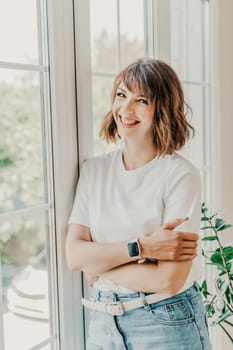 Office window woman. Business woman standing in the office with her arms crossed near the window. Dressed in a white T-shirt and jeans