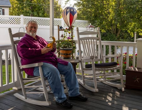 A Senior Aged Male Resting in a Rocking Chair, on a Deck, Enjoying His Retirement Wondering What He is Holding, on a Autumn Day