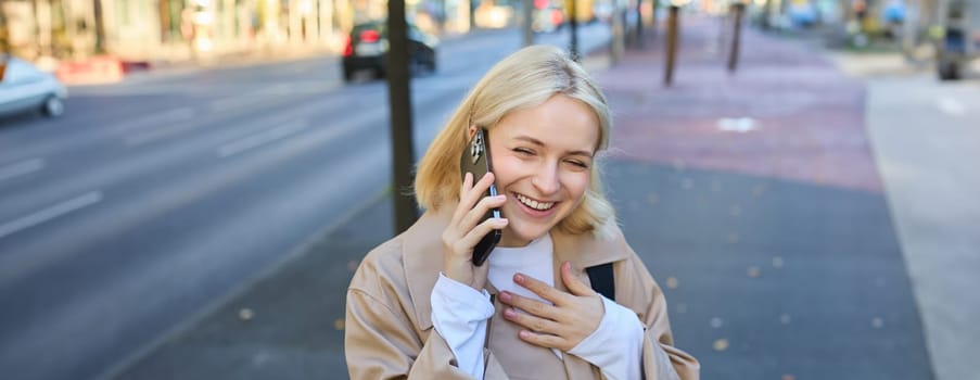 Close up portrait of modern young woman, laughing and smiling, walking along the street and answer phone call, chatting on mobile telephone, has funny conversation on her way home.