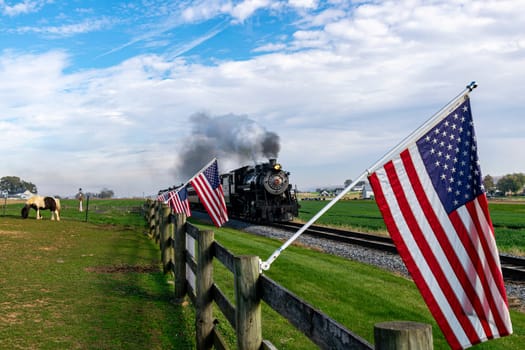 Ronks, Pennsylvania, November 4, 2023 - View of an Antique Steam Passenger Train Approaching With a Line of American Flags, Blowing Smoke on a Fall Day