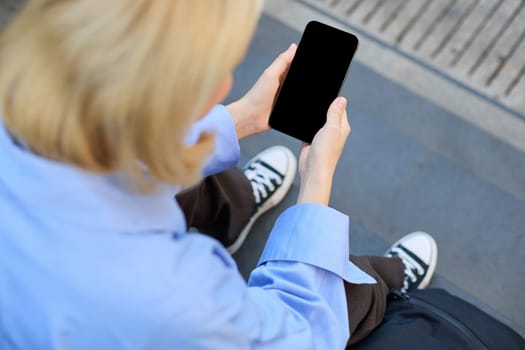 Close up of woman looking at smartphone, cropped shot of mobile phone in female hands, girl sitting on stairs and using telephone.
