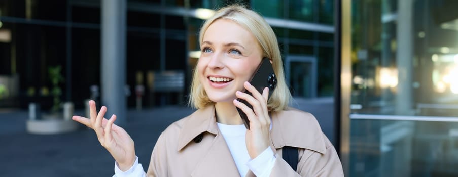 Close up portrait of young blond woman, walking on street and talking on mobile phone, chatting with friend on smartphone. Lifestyle and people concept