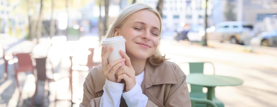 Close up portrait of smiling, happy beautiful european woman, sitting in cafe and enjoying cup of coffee, drinking beverage, enjoying bright sunny day outdoors.