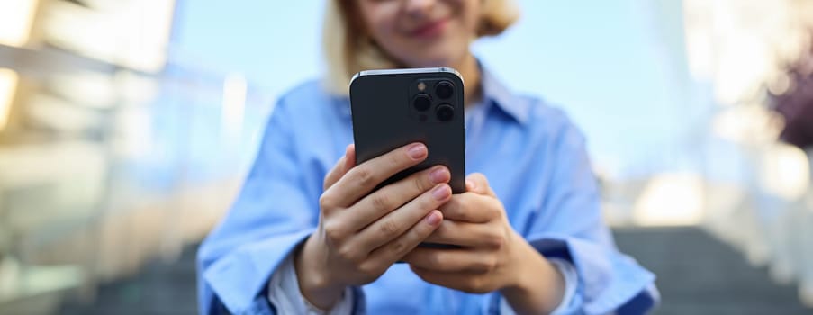 Close up portrait of smartphone in hands of young woman, who sits and rests on stairs outdoors. Technology and people concept
