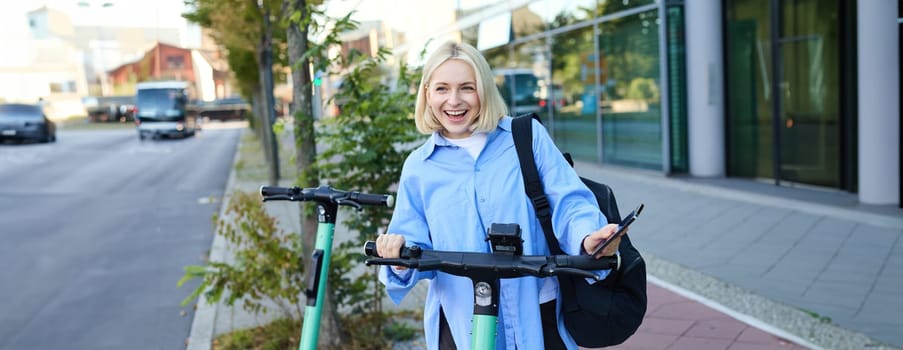 Portrait of young smiling woman, unlocks electric scooter, scans qr code with smartphone app to unlock her ride, standing on street near building.