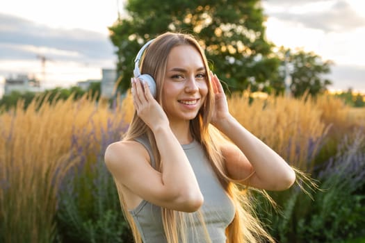Blonde young woman listening music using headphones while resting in the park.