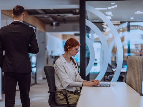 A young businesswoman with orange hair sitting confidently, fully engaged in her work on the laptop, exuding creativity, ambition, and a vibrant sense of individuality.