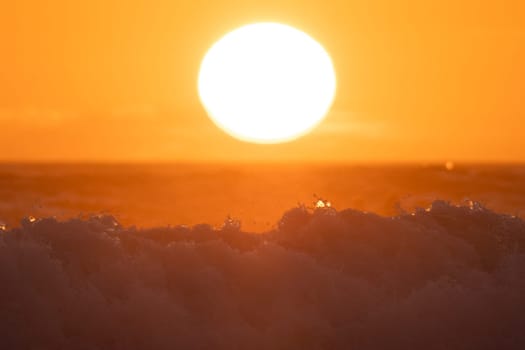 Big sea wave under huge bright sun at orange sunset. Mid shot