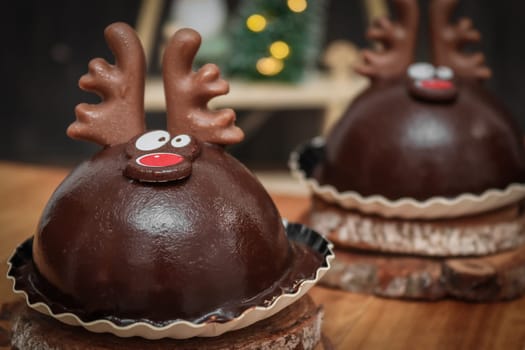 Two chocolate deer on wooden cuts and on a tray with christmas decoration on the table, side view close-up.