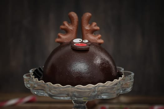 One chocolate deer in a glass cake bowl on a brown wooden table, close-up side view.