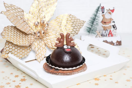 Two chocolate deer cakes in a white wooden tray with christmas decoration on the table, side view close-up.